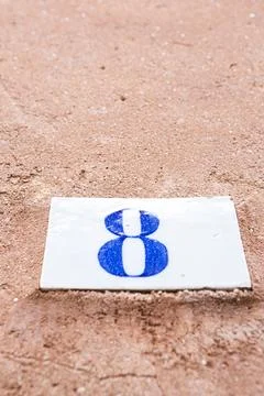 Square white ceramic brick on old wall with the number eight painted in blu.. Stock Photos