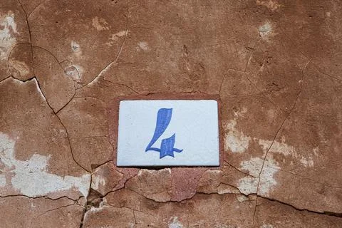 Square white ceramic brick on old wall with the number four painted in blue.. Stock Photos
