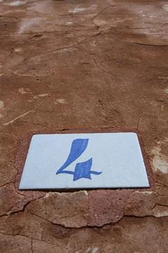 Square white ceramic brick on old wall with the number four painted in blue.. Stock Photos
