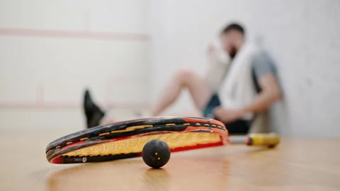 Squash racket and ball lie on floor near resting sportsman Stock Footage 221002334
