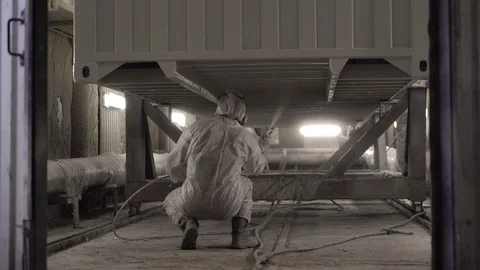 The squatting worker paints the bottom of the container. 4K Stock Footage 104656883