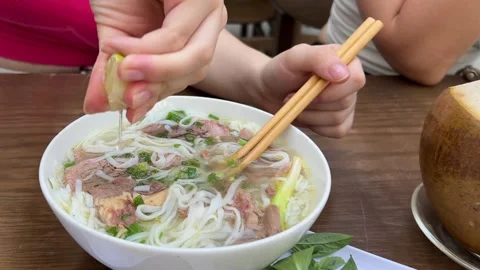 Squeeze into lime soup hand squeezes lime over a bowl of pho in a bustling Stock Footage 308305707