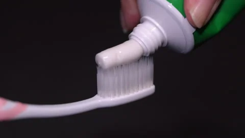 Squeeze a white toothpaste from a tube onto a toothbrush, black background.v Stock Footage 227855218