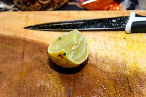 A squeezed half lime with seeds sitting on a wooden cutting board alongside.. Stock Photos