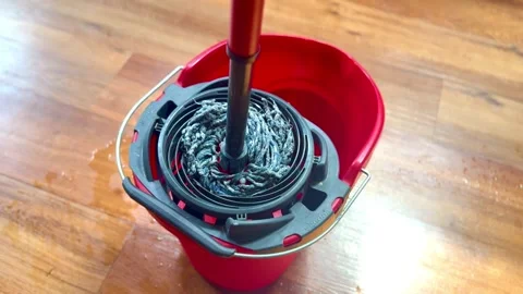 Squeezing and draining water liquid from wet mop into red bucket with wood floor Stock Footage 340434874