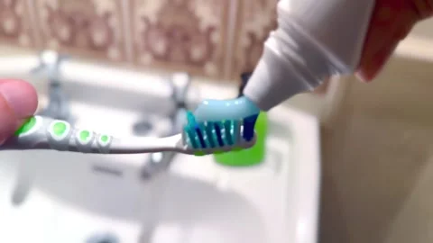 Squeezing blue toothpaste onto green and white toothbrush next to bathroom sink Vídeos de archivo 333939736