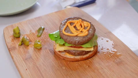 Squeezing cheese sauce onto a beef burger patty on a wooden cutting board i.. Видео 346800370