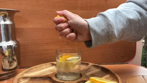 Squeezing Fresh Lemon Juice into Glass of Water on Wooden Tray Stock Footage 332497351