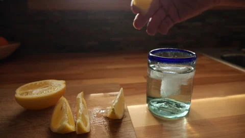 Squeezing a fresh lemon slice into a cool glass of ice water Stock Footage 236409882