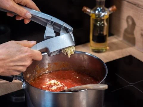 Squeezing garlic with a special metal squeezer, kitchen cooking tomato sauc.. Stock Photos