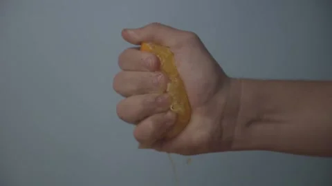 Squeezing Half an Orange Against a Blue Background Juice Spray LOG Stock Footage 136992457