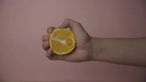 Squeezing Half an Orange against a Pink background LOG Stock Footage 136992477