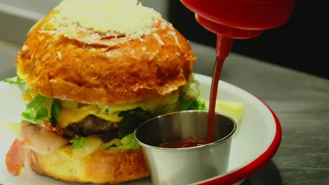 Squeezing ketchup into metal cup to serve burger on plate Video stock 325057901