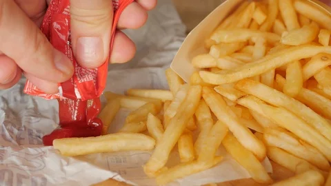 Squeezing ketchup out of a plastic packet, sachet next to a portion of fries Stock Footage 126026913