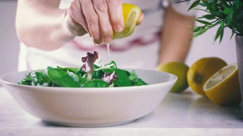 Squeezing lemon on fresh salad. Chef preparing a dish full of green leaves  Stock Footage 146921684