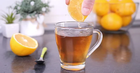 Squeezing Lemon into Hot Tea in Mug on Kitchen Counter Video stock 327543114