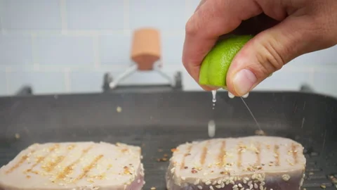 Squeezing a lime juice over a steak of yellowfin tuna on a grilling pan in 4K. Stock Footage 154459353