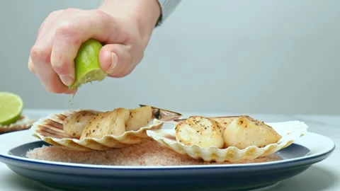 Squeezing lime juice on top of freshly fried scallops into a shell in a plate. Stock Footage 142689728