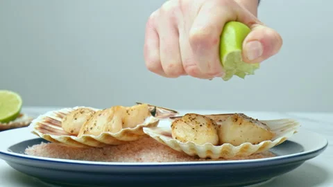 Squeezing lime juice on top of freshly fried scallops into a shell in a plate. Stock Footage 142690966