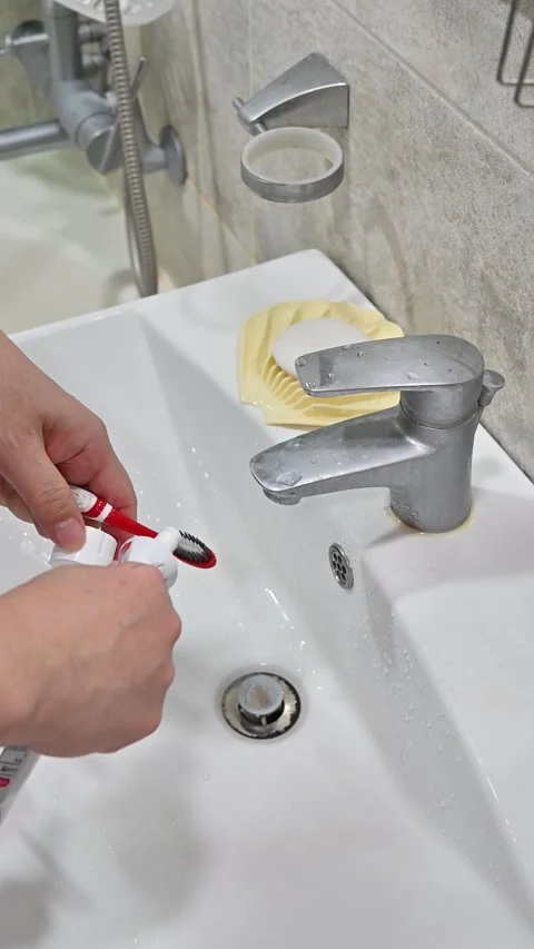 Squeezing toothpaste onto toothbrush at bathroom sink 스톡 동영상 328229827