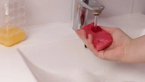 Squeezing a wet sponge under running water in a sink, showing hand pressure.. Stock Footage 321833601