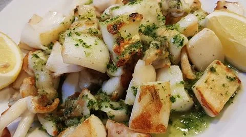 Squid in small pieces cooked in a pan and seasoned with lemon slices Foto stock