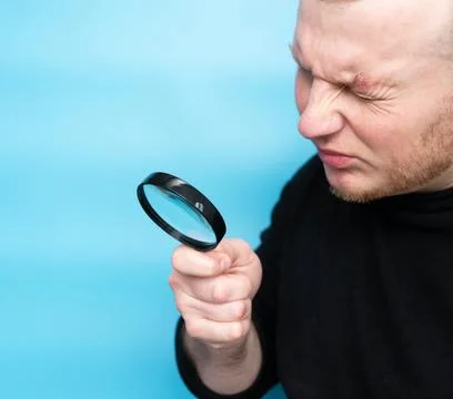 Squinting while reading the text through a magnifying glass, a young man ha.. Stock Photos