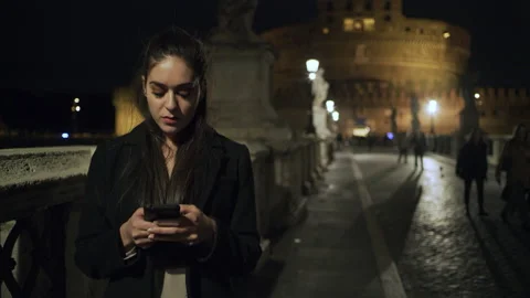 On the St Angelo Bridge at night, a young Italian woman stands texting on her ph Stock Footage 199457322