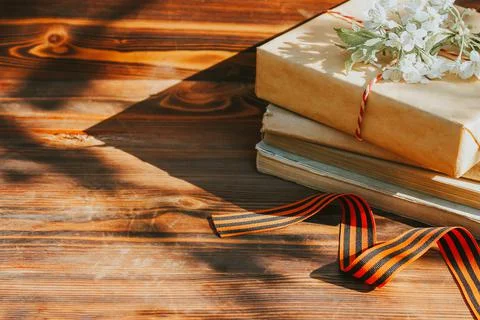 A St. George ribbon and a stack of old books on a wooden background with a sp 库存照片