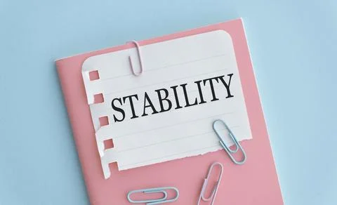 Stability text on white paper on blue background, pink notebook. Stock Photos