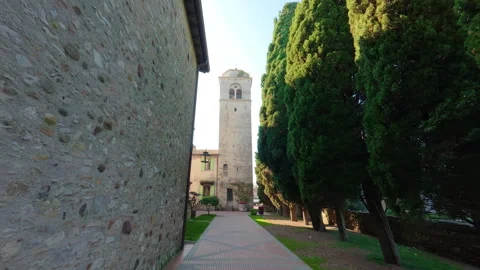 Stabilized forward walk along medieval church path with trees and brick bell tow Stock Footage 322101482