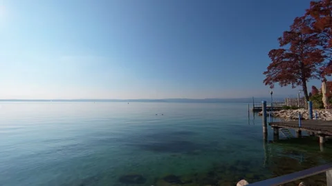 Stabilized left-to-right move along lake shore with pier and distant coast at su Stock Footage 322104869