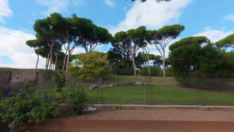 Stabilized right-to-left walk past manicured garden with Roman ruins behind fenc Stock Footage 322112305