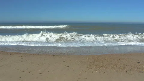 Stable shot slowly pulling back from the waves crashing on a empty, golden Stock Footage 133576616