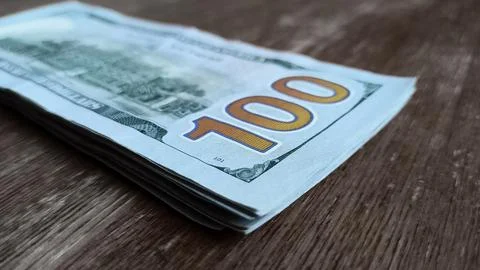 Stack of 100 dollar bills rests on a wooden table Foto stock