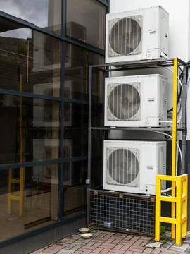 A stack of air conditioners sitting on top of each other in front of a building Stock Photos