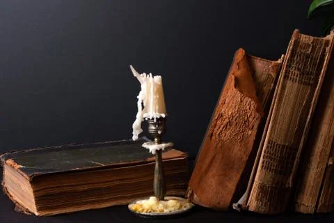 Stack of ancient books and bronze candlestick with candle Stock Photos