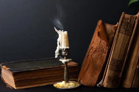 Stack of ancient books and candlestick with steaming candle Stock Photos