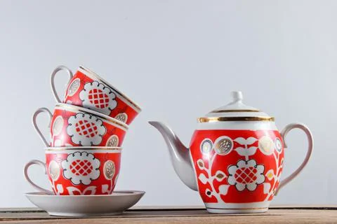 Stack of antique ceramic cups and teapot on wooden table against a white wall Stock Photos