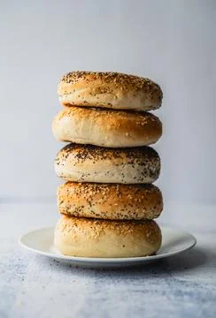 Stack of assorted bagels on plate against light background. Stock Photos