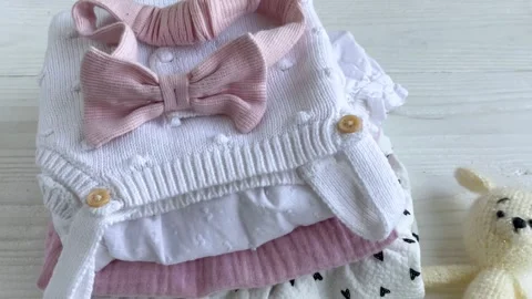 Stack of baby clothes, pink headband and knitted toy bunny. Stock Footage 274474233