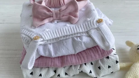 Stack of baby clothes, pink headband and knitted toy bunny. Stock Footage 274699997