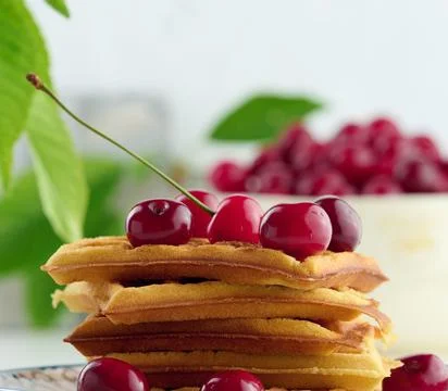 Stack of baked Belgian waffles with ripe red cherries on the white table, bre Stock Photos