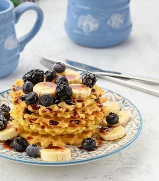 Stack of baked Belgian waffles on a round plate with berries on a white table Stockfoto's