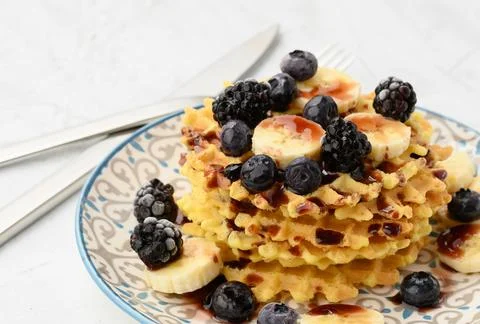 Stack of baked Belgian waffles on a round plate with berries on a white table Foto stock