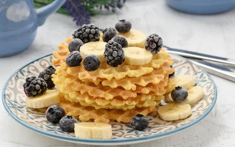 Stack of baked Belgian waffles on a round plate with berries on a white table Stock-Fotos