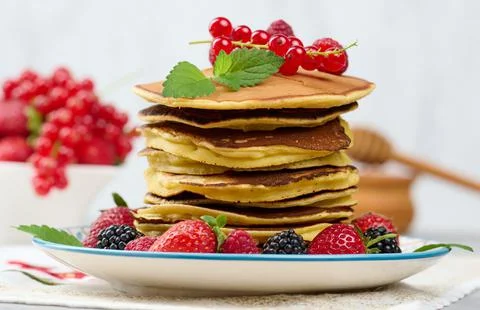 Stack of baked pancakes with fruits in a round plate on a white table Foto stock