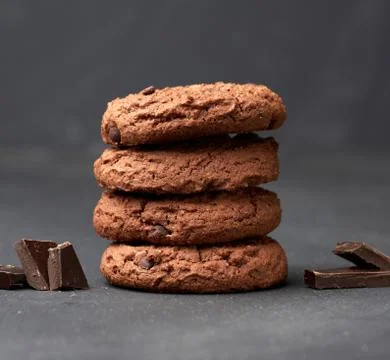 Stack of baked round chocolate chip cookies and pieces of chocolate on a blac Stockfoto's