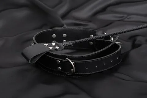 Stack for bdsm games and leather collar on black silk background. Stock Photos