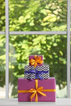 Stack of beautifully wrapped gift boxes on white table  near window. Space fo Stock Photos